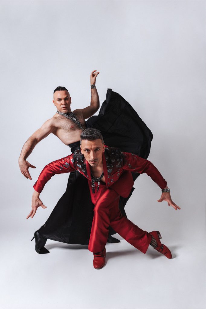 A dancer in red beneath a black cape swept wide, pale studio ground.